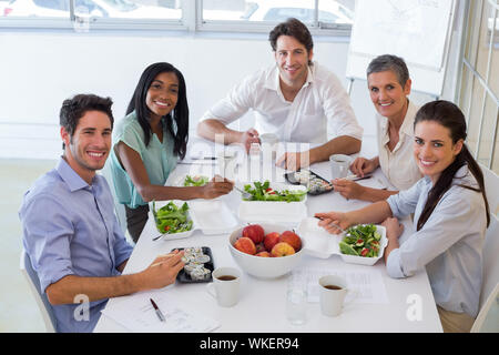 Lavoratori sorriso alla telecamera mentre mangiare sano il pranzo in ufficio Foto Stock