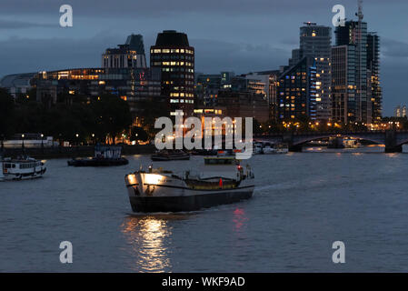 Polla Rose nave trasporto barca con lo skyline di Londra al tramonto con luci per gli edifici di sera. Il fiume Tamigi del traffico fluviale. Notte. Dark Foto Stock