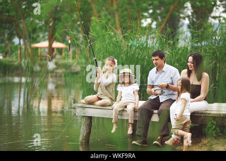 Giovane famiglia felice con i ragazzi con attività di pesca in stagno in estate Foto Stock