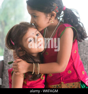 Indian ragazza baciare la sua sorella più giovane con l'amore. Famiglia asiatica a casa. Belle figlie in India tradizionale sari. Foto Stock
