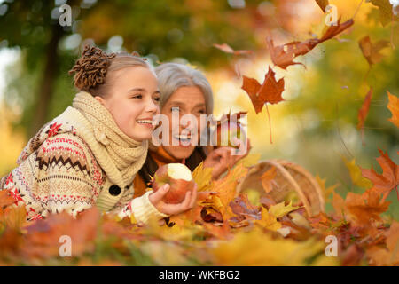 La ragazza con la nonna giacente su erba, vicino a cesto in vimini pieno di mele nel parco autunnali Foto Stock