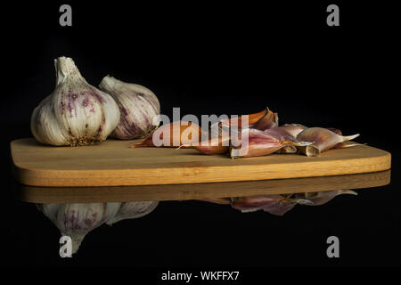 Gruppo di due intero lotto di pezzi di organico aglio bianco allium sativum sul bambù tagliere isolato sul vetro nero Foto Stock