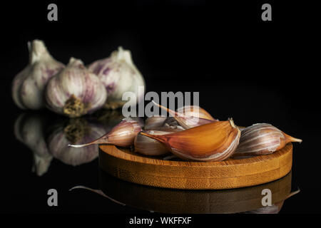 Gruppo di tre intero lotto di pezzi di organico aglio bianco allium sativum sul bambù coaster isolato sul vetro nero Foto Stock