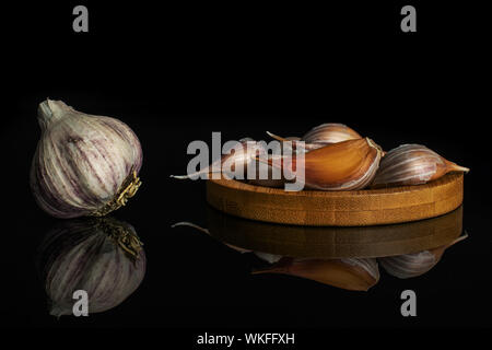 Un intero lotto di pezzi di organico aglio bianco allium sativum sul bambù coaster isolato sul vetro nero Foto Stock