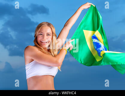 Felice fan del calcio brasiliano squadra, allegro Pretty girl su stadium il tifo nel supporto, mantenendo la grande bandiera nazionale del Brasile, le persone attive trave Foto Stock