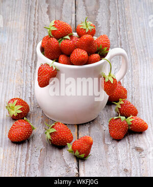 Fresche e mature le fragole di bosco in tazza da tè isolati su rustico sfondo di legno Foto Stock