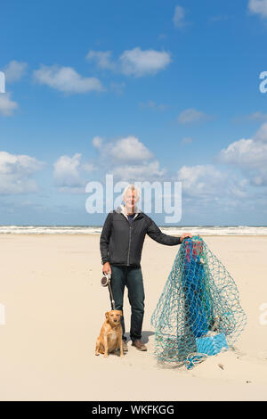 L'uomo con il cane vicino al palo di legno sulla spiaggia di wadden olandese isola Terschelling Foto Stock