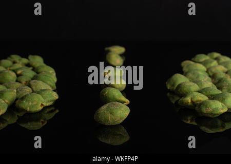 Sacco di tutta verde piccante wasabi peanut facendo una linea tra due gruppi isolati su vetro nero Foto Stock
