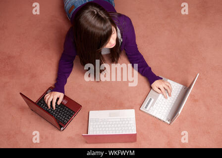 Giovane donna multitasking con tre laptop sdraiato sul pavimento Foto Stock