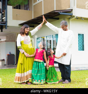 I genitori casa di formatura forma del tetto al di sopra dei bambini. Bella asiatica famiglia indiana ritratto sorridente e in piedi al di fuori della loro nuova casa. Foto Stock