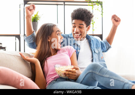 Giovane nero giovane celebrando la vittoria della squadra di calcio preferita, guardare lo sport a casa Foto Stock