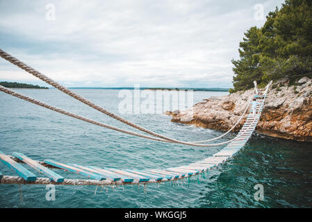 Donna attraversando ponte sospeso sul mare sullo sfondo Foto Stock