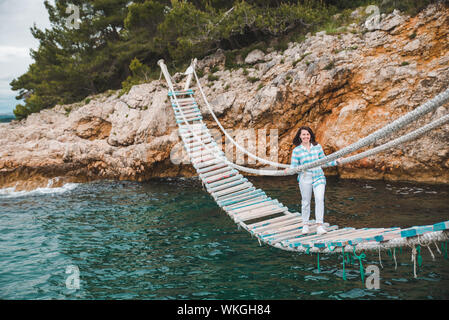 Donna attraversando ponte sospeso sul mare sullo sfondo Foto Stock