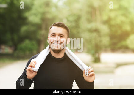 Uomo sorridente in appoggio dopo allenamento con asciugamano intorno al suo collo Foto Stock