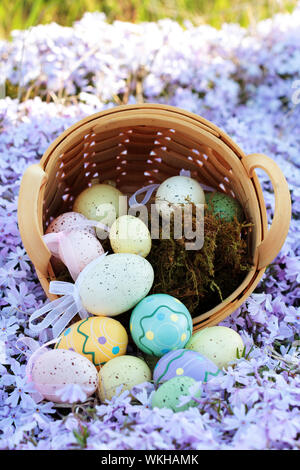 Le uova di pasqua di fuoriuscita da un cesto in un letto di fiori di primavera. Messa a fuoco selettiva centro sulla porzione di immagine in cui le uova sono fuoriuscita con estrema s Foto Stock