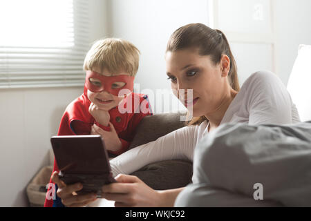 La madre e il bambino supereroe di giocare ai videogiochi insieme nel soggiorno. Foto Stock