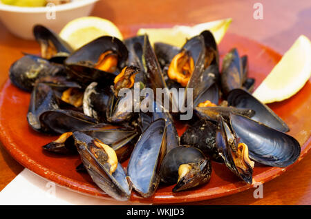 Cucinato fresco bollito di cozze in conchiglie sulla vecchia piastra servita con il limone su sfondo di legno Foto Stock