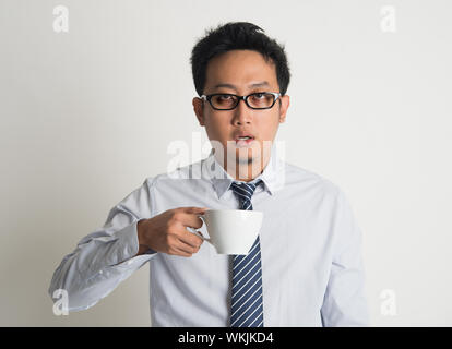 Stanco Asian imprenditore con occhi scuri cerchio holding tazza da caffè su sfondo semplice Foto Stock