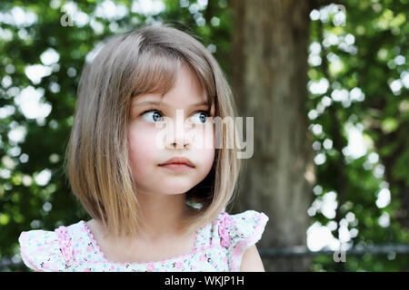 Carino bambina con bobbed taglio capelli cercando di distanza dalla fotocamera. Estrema profondità di campo. Foto Stock