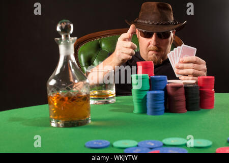 Foto di un uomo giocando a poker indossando occhiali da sole e un cappello. Foto Stock