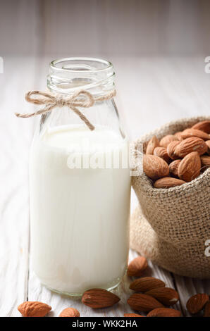 Latte o yogurt in una bottiglia di vetro bianco sul tavolo di legno con le mandorle nel sacco di canapa a parte Foto Stock