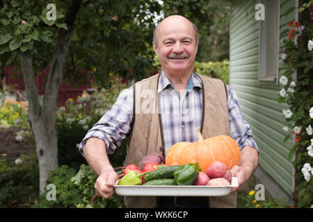 Sorridente uomo maturo con verdure raccolte nel suo giardino. Eco Friendly farm concetto. Foto Stock