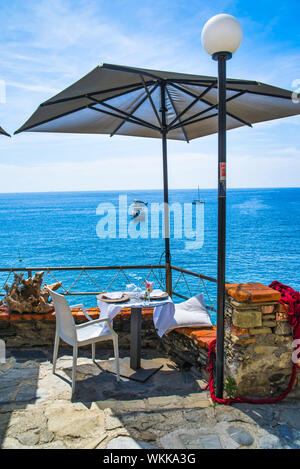 Monterosso al Mare, Italia - Agosto 17, 2019: tabella sotto un ombrellone in una caffetteria sulla montagna / vista mare con barche e yacht / Cinque Terre Foto Stock