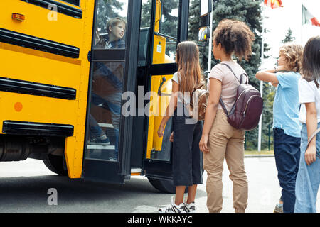 Un gruppo di compagni di scuola i bambini che vanno a scuola in autobus in piedi vicino a porta in coda vista laterale Foto Stock