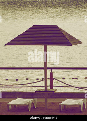 Sedie e parasole della spiaggia in giorno nuvoloso all'esterno. In stile retrò Foto Stock