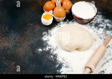 Materie la pasta lievitata in una terrina e ingredienti, uova, farina, spighe di grano scuro sul tavolo di cucina e panetteria concetto, Foto Stock