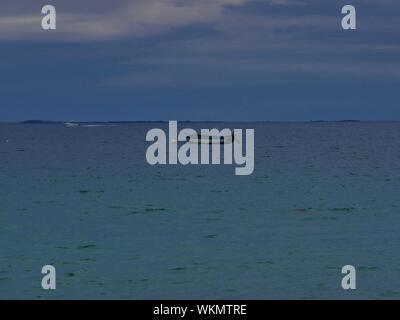 Barca bleue et blanche , ancrée devant la plage de plouguerneau , en arrière plan une île deserte , eau bleue turchese Foto Stock