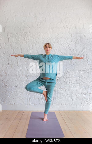 Ragazza incinta in un blu tuta sportiva sorge nello yoga pone a piena lunghezza ritratto Foto Stock