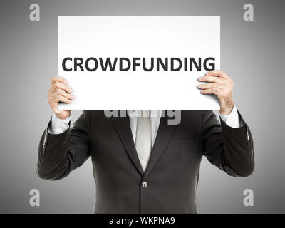 Un business man in possesso di una carta nella parte anteriore del suo volto con il testo crowdfunding Foto Stock