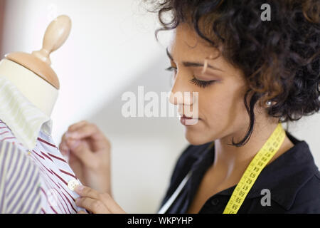 I giovani ispanici sarta femmina pulsante cucitura su magliette su sartoria manichino. Foto Stock
