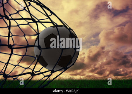 Immagine composita del calcio nel retro del net contro erba verde sotto il cielo nuvoloso Foto Stock