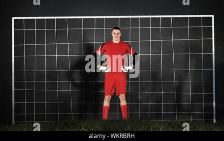 Immagine composita di portiere in rosso guardando la telecamera contro obiettivo net Foto Stock