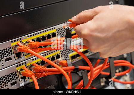 Maschio Ingegnere IT collegando il cavo di rete nel router in Datacenter Foto Stock