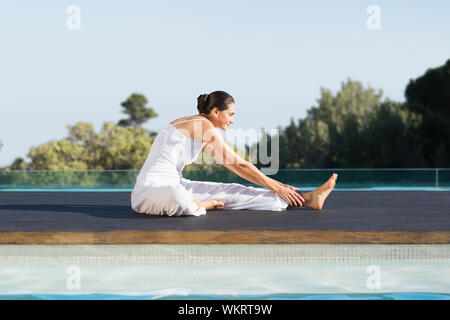 Bruna pacifica in janu sirsasana yoga pongono a bordo piscina su una soleggiata giornata alle terme Foto Stock