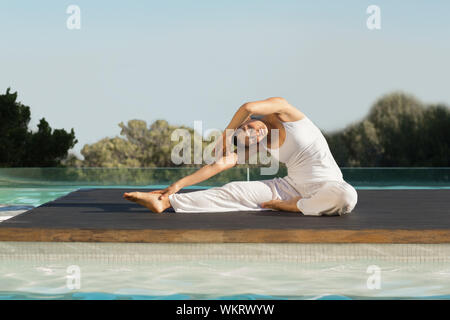 Bruna pacifica in janu sirsasana yoga pongono a bordo piscina su una soleggiata giornata alle terme Foto Stock