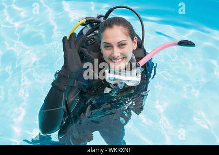 Donna sorridente sulla formazione di scuba in piscina facendo segno ok in una giornata di sole Foto Stock