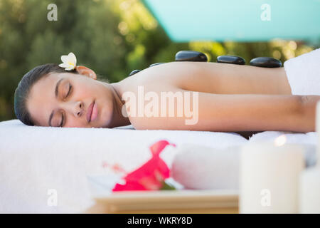 Sorridente brunette giacente su asciugamano avente un massaggio hot stone al di fuori alla spa Foto Stock