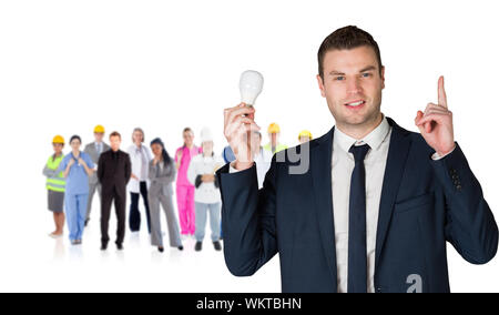 Immagine composita di imprenditore tenendo la lampadina della spia e rivolta contro il gruppo dei lavoratori Foto Stock