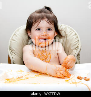 Happy baby divertirsi mangiando sudicie coperte in Spaghetti Angel Hair Pasta marinara rosso salsa di pomodoro. Foto Stock