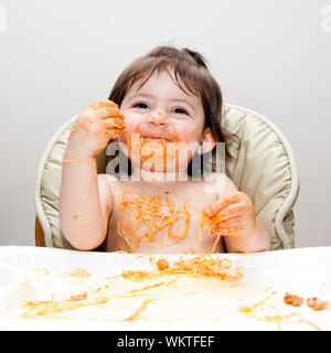 Sorridenti baby divertirsi mangiando sudicie coperte in Spaghetti Angel Hair Pasta marinara rosso salsa di pomodoro. Foto Stock