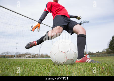 Il portiere in rosso calci palla lontano dal traguardo in un giorno chiaro Foto Stock