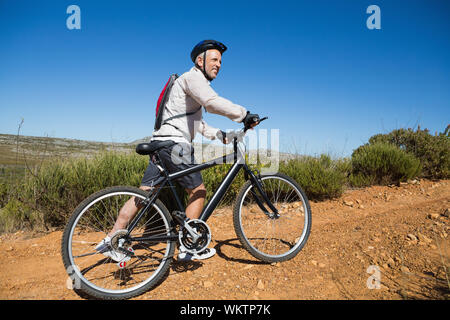 Montare il ciclista spingendo bike in salita su del terreno di campagna in una giornata di sole Foto Stock