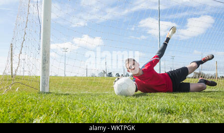 Il portiere in rosso effettuare un salvataggio in un giorno chiaro Foto Stock