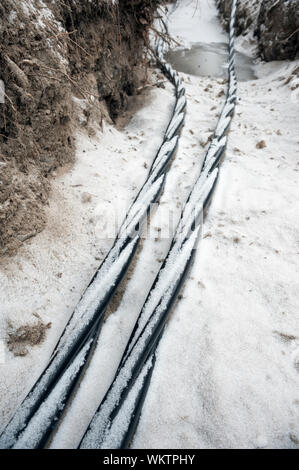 La posa di una fibra ottica e cavi di energia elettrica nel suolo ghiacciato, cavi interrati per internet veloce nella regione rurale - cablaggio sotterraneo in Finlandia Foto Stock