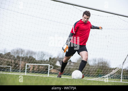 Il portiere in rosso calci palla lontano dal traguardo in un giorno chiaro Foto Stock