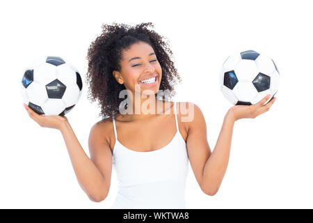 Pretty girl holding palloni da calcio e sorridente alla fotocamera su sfondo bianco Foto Stock